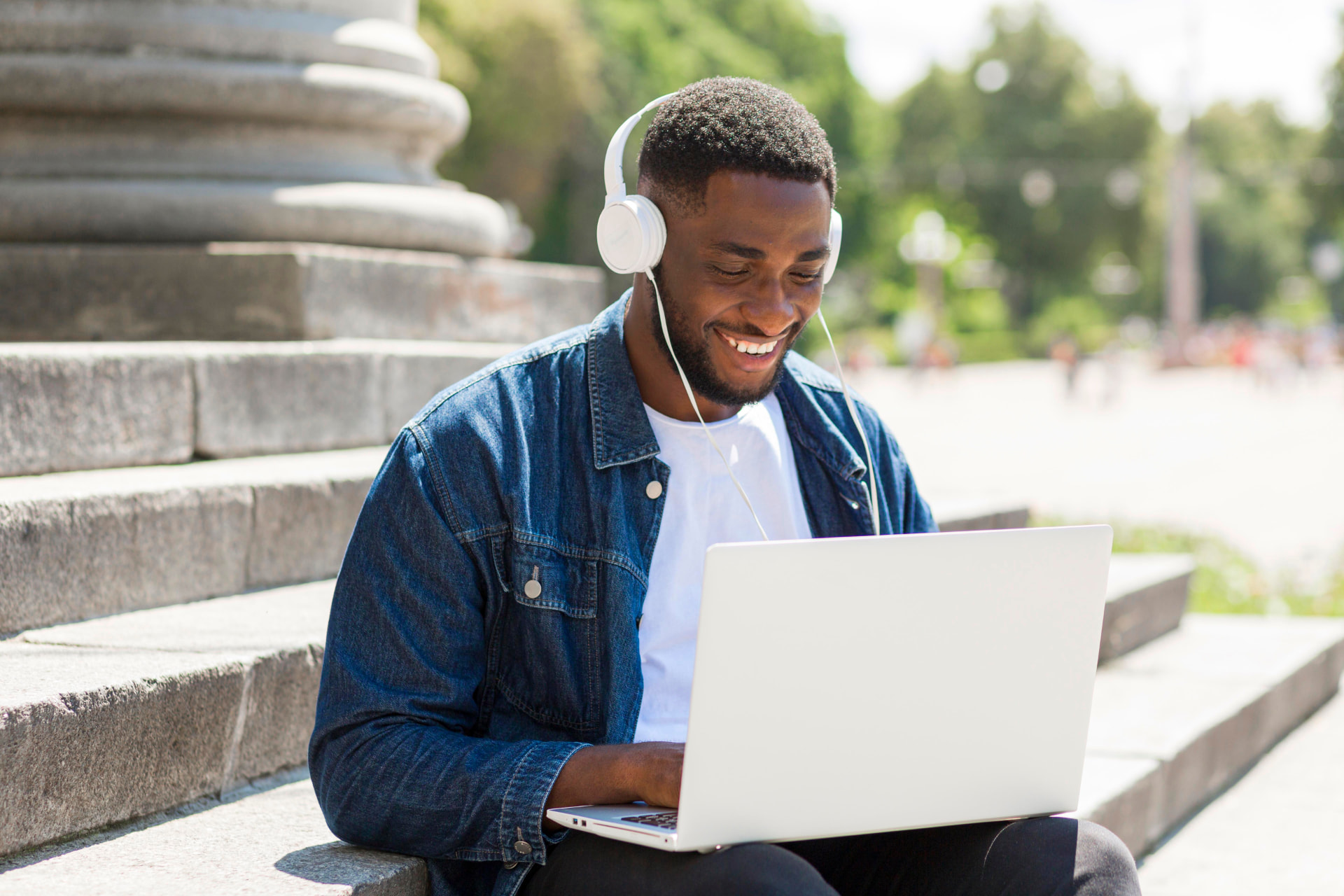 Student smiling while working on a laptop on campus steps